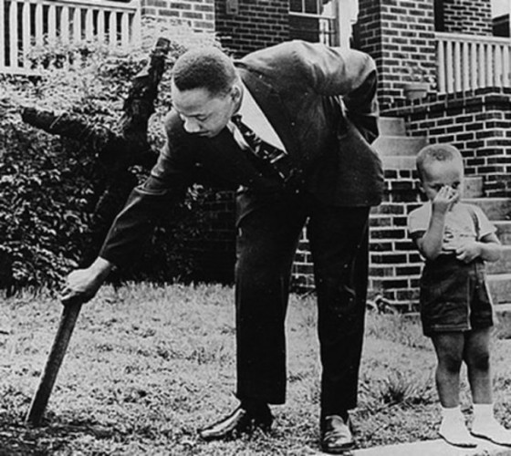 Martin Luther King removing a burnt cross from his front lawn as his 5-year-old son looks on.